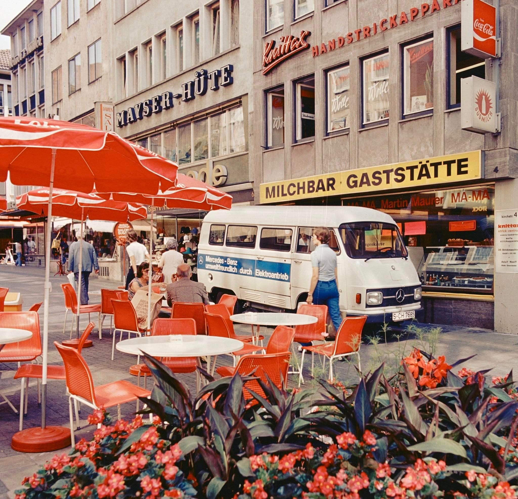 Historische Aufnahme eines Mercedes-Benz Elektrotransporters mit der Aufschrift „umweltfreundlich durch Elektroantrieb“ in einer Fußgängerzone